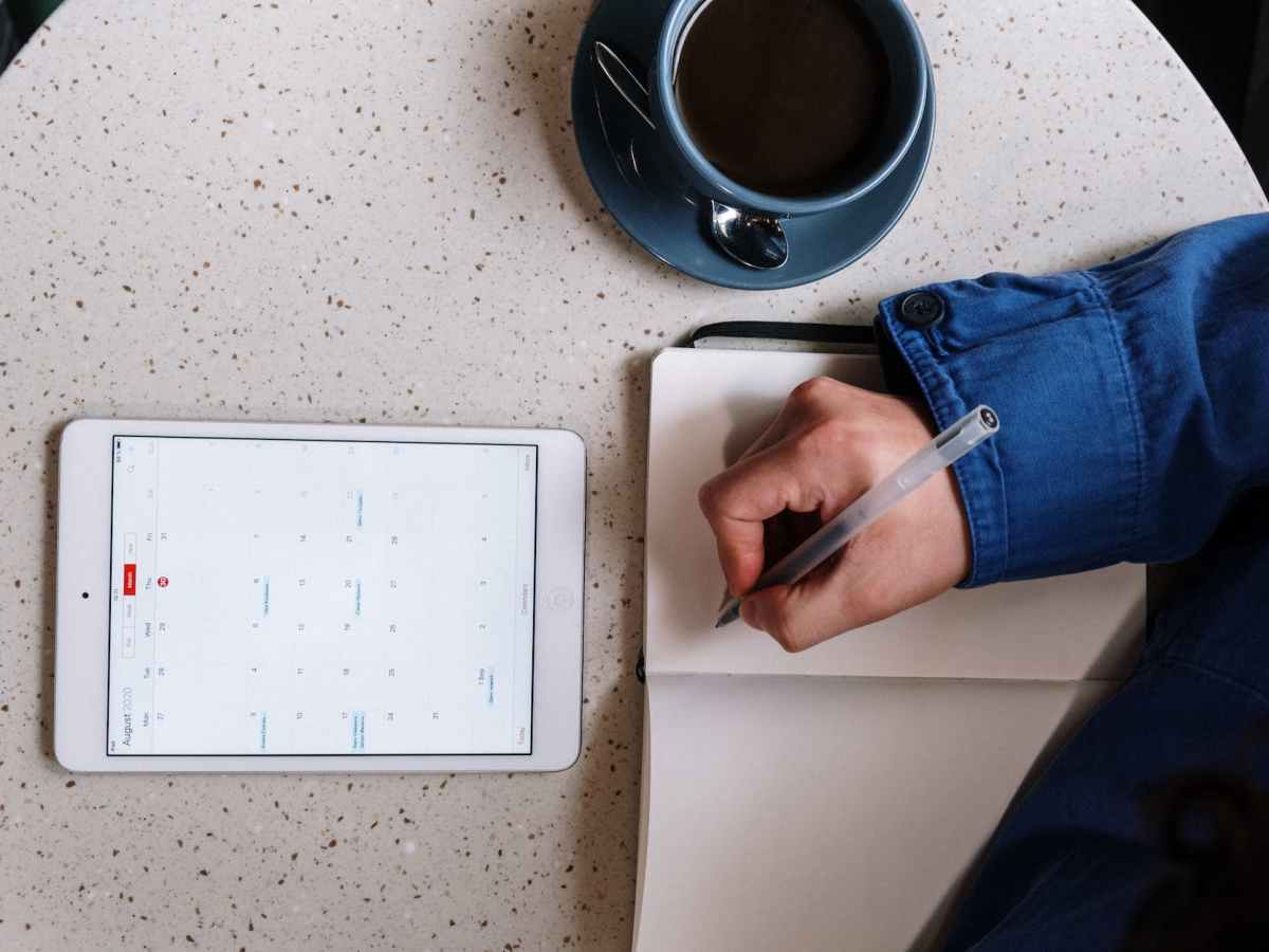 person holding pen and checking calendar on tablet