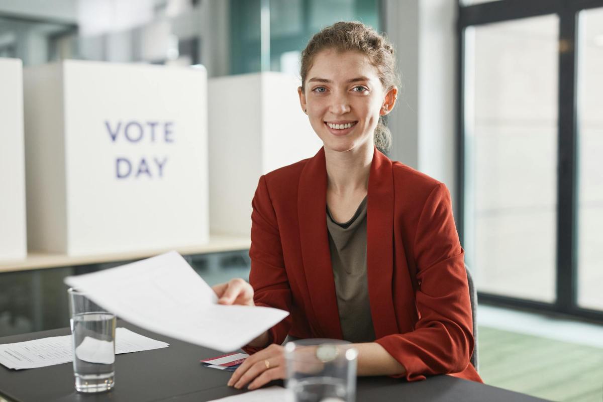 a woman in red blazer smiling and holding a white paper