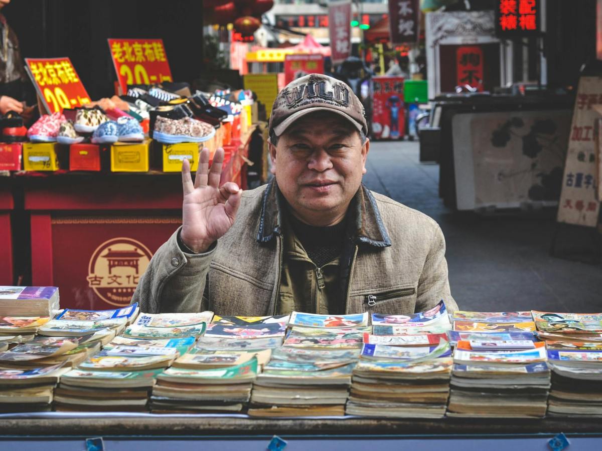 man in brown coat in front of books