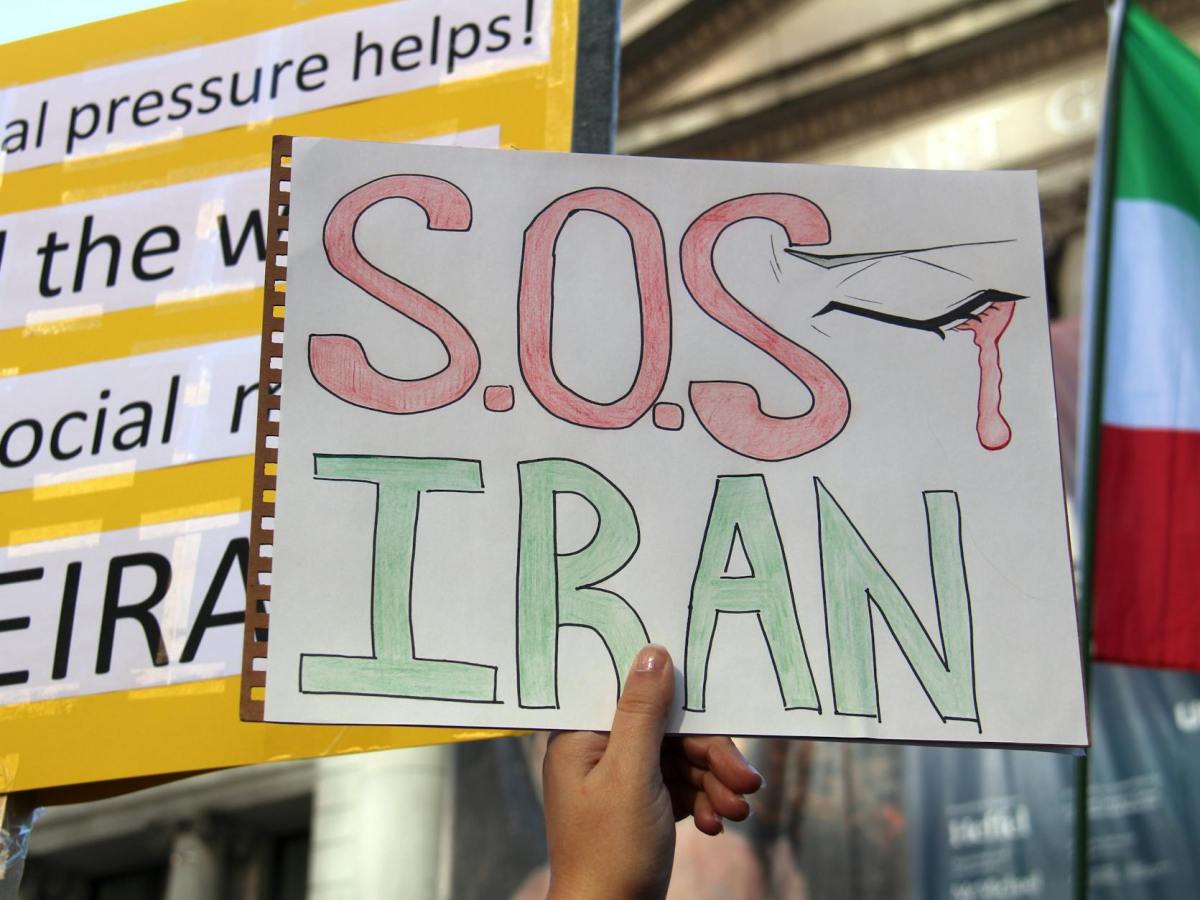a person holding a placard with an s o s iran message