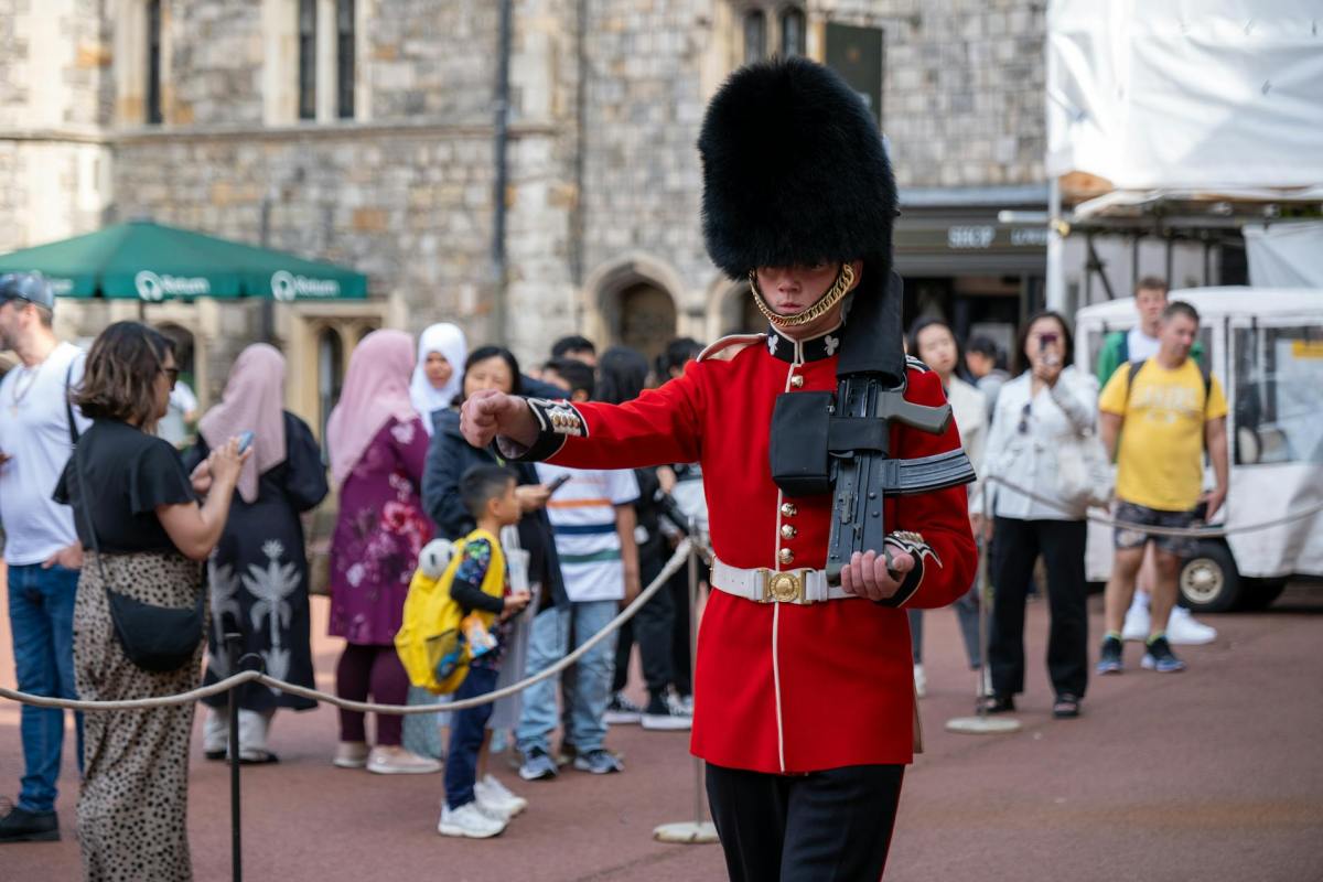 tourists watching a kings guard marching with an assault rifle
