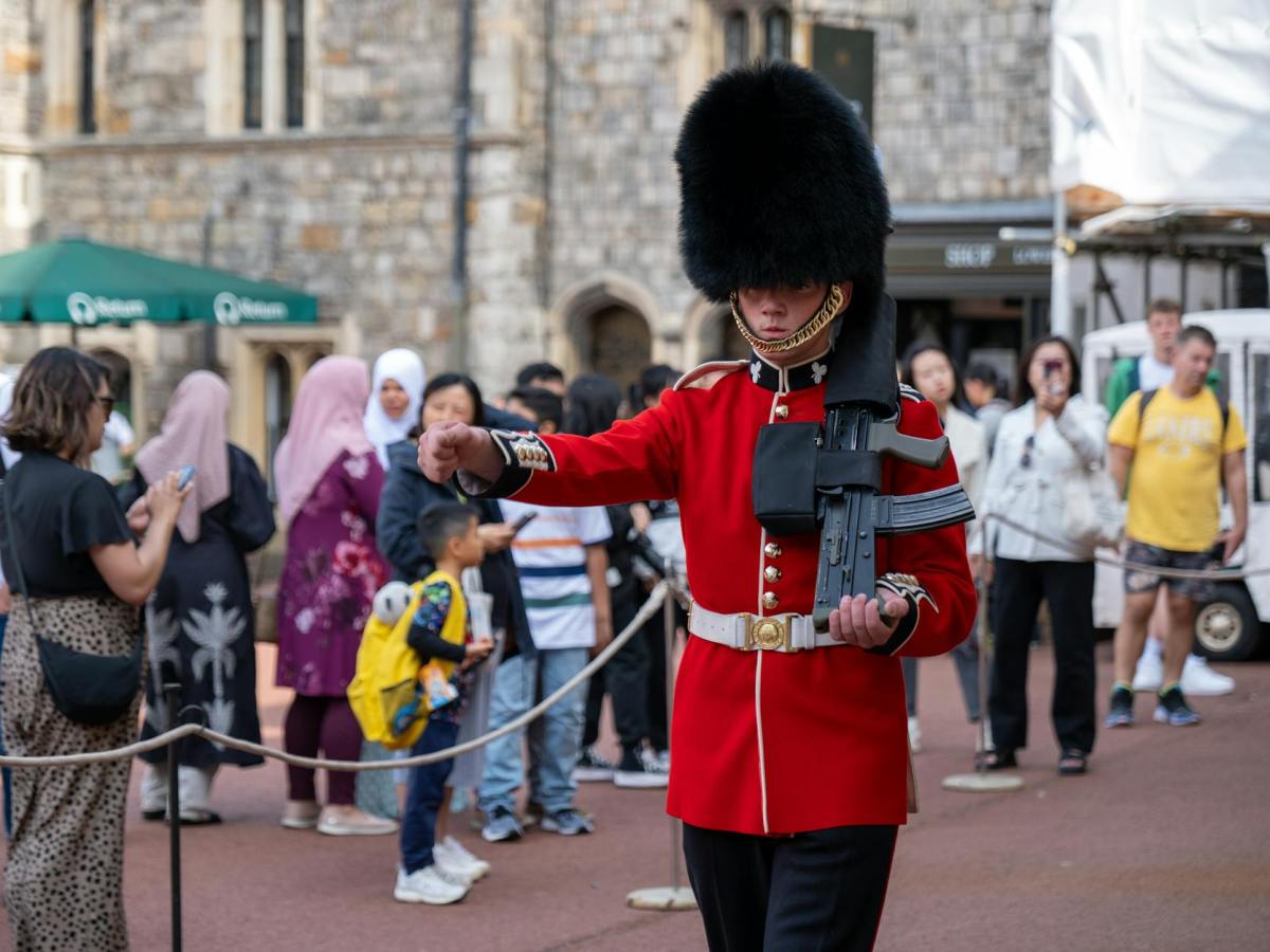 tourists watching a kings guard marching with an assault rifle