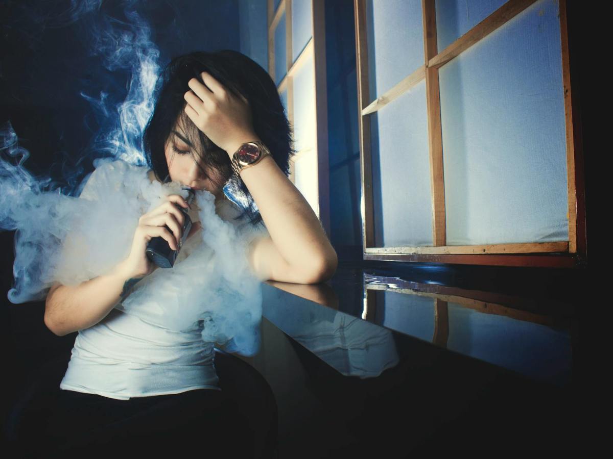young woman smoking e cigarette in darkness