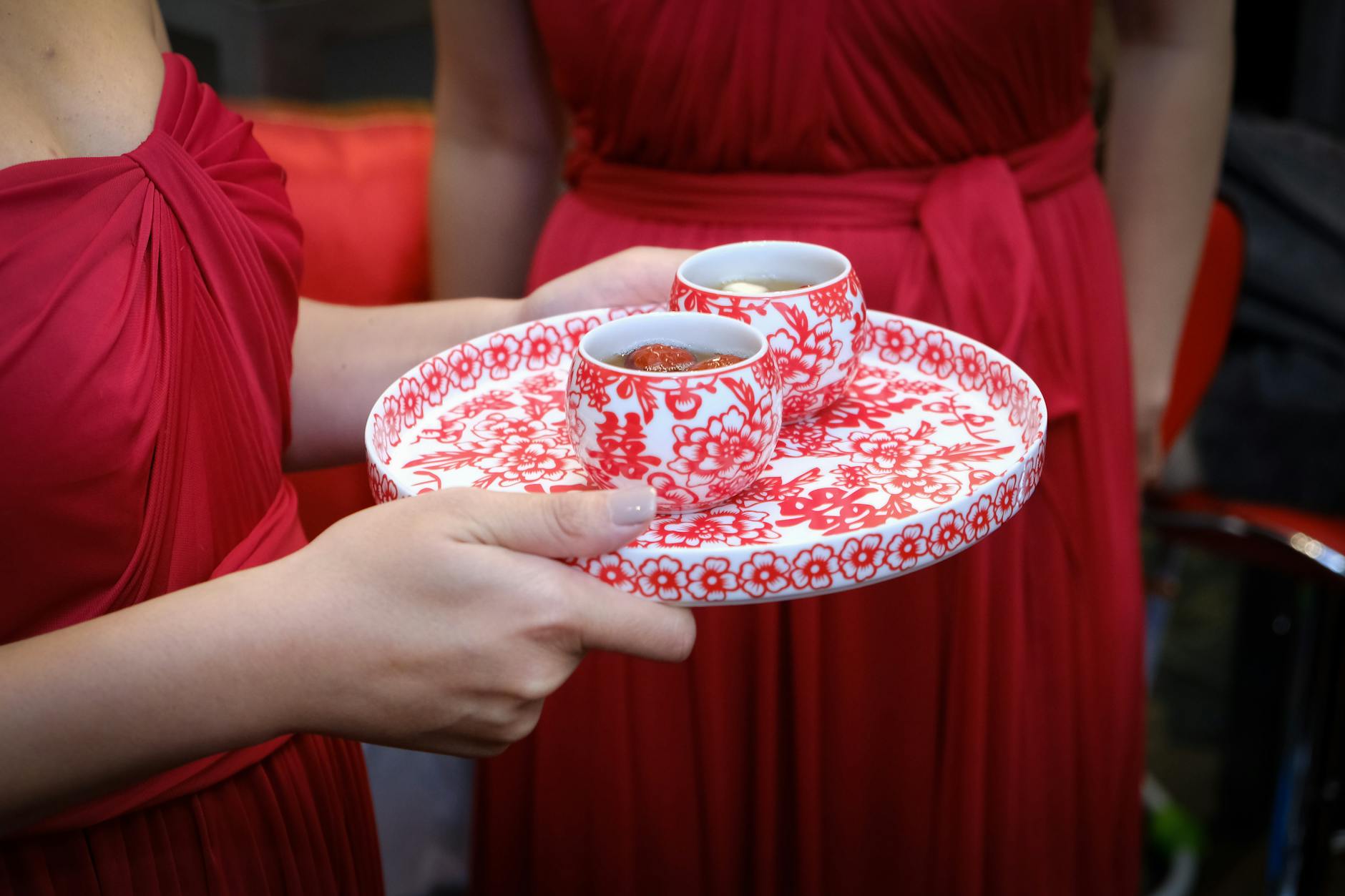 close up of woman in red dress holding a tray with ceramic cups