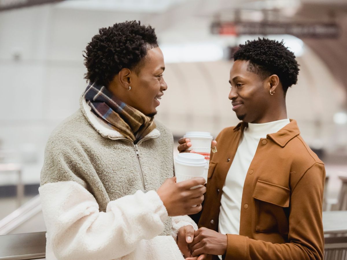 cheerful black homosexual couple with coffee talking in subway